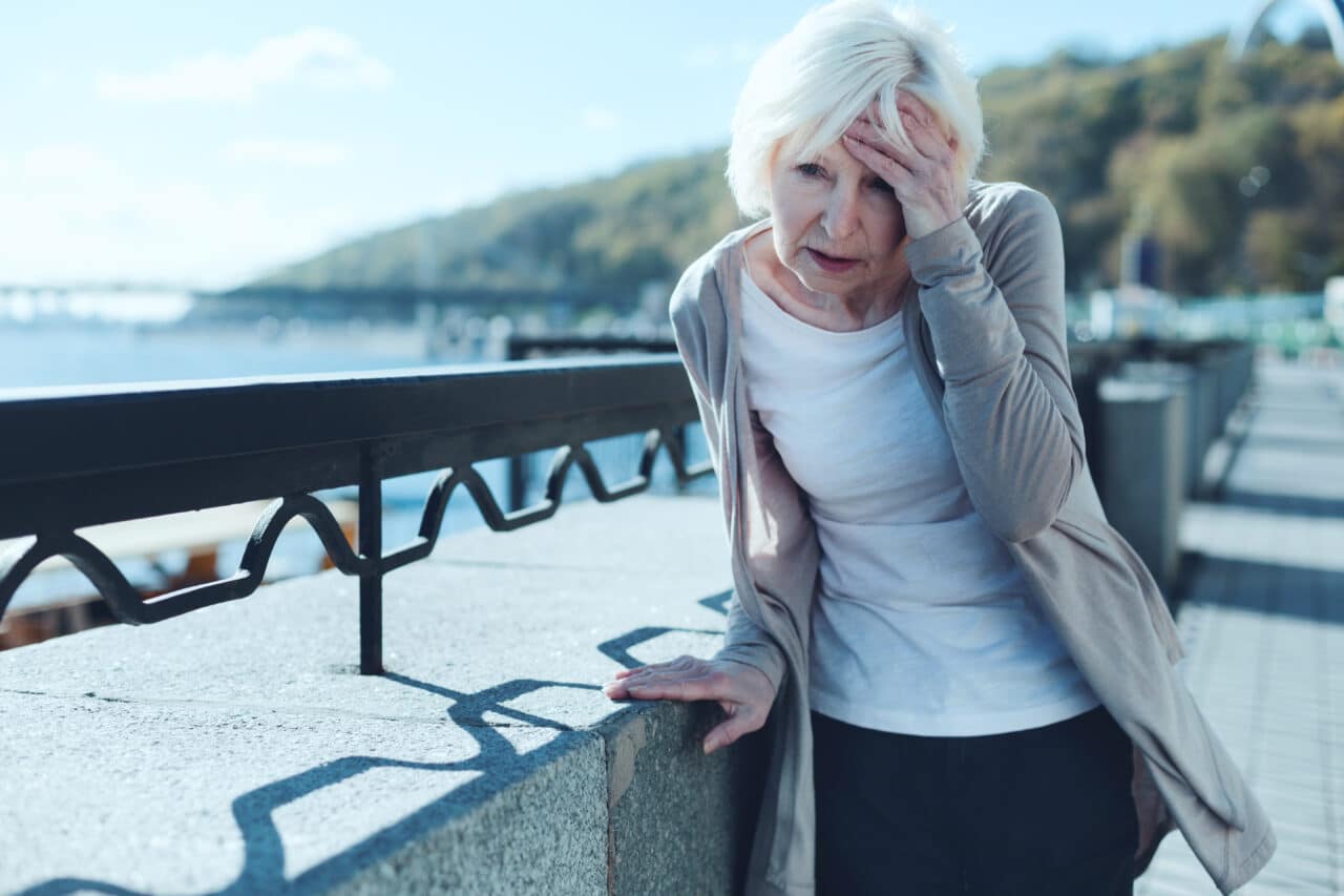 Senior woman feeling dizzy while out for a walk by the water.