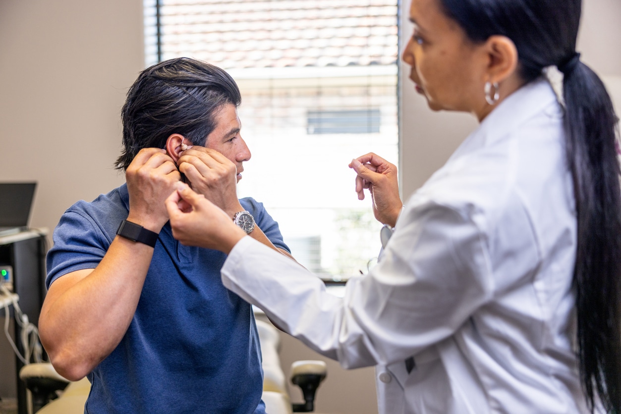 Man at a hearing aid service appointment taking out his hearing aid to show the doctor.