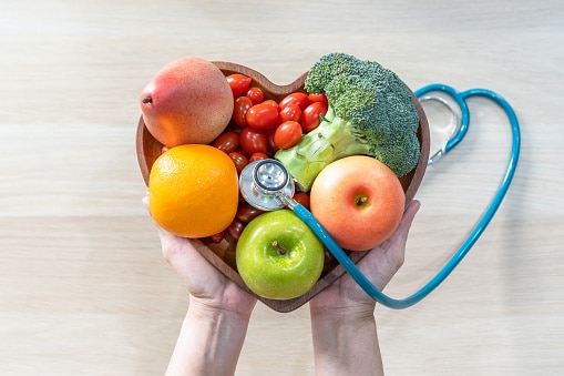 Hands holding a heart-shaped bowl of vegetables with a stethoscope.