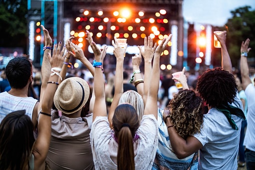Rear view of large group of friends having fun with raised arms on a music festival.