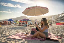 Woman sitting on the beach playing on her phone.