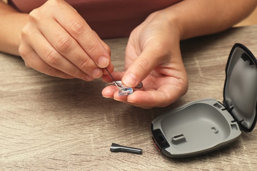 A close-up of a person's hands using a specialized cleaning brush to maintain a behind-the-ear hearing aid device for better performance and hygiene.