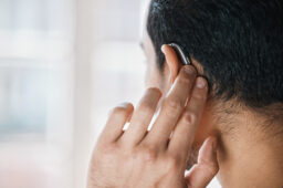 Rear shot of a man touching his behind-the-ear hearing aid.