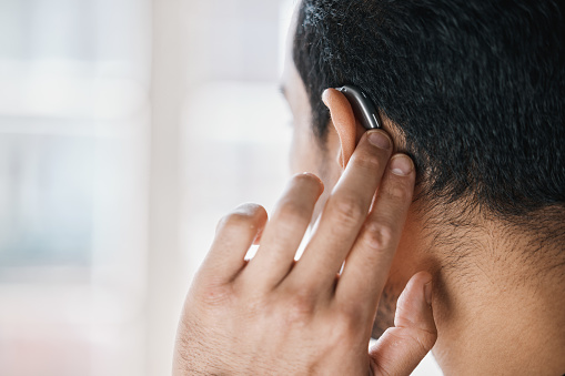Rear shot of a man touching his behind-the-ear hearing aid.