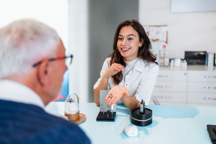 Audiologist is presenting a hearing aid device to a patient during a consultation in an audiology clinic.
